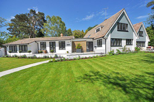 A modern house with a large green lawn under a clear blue sky.