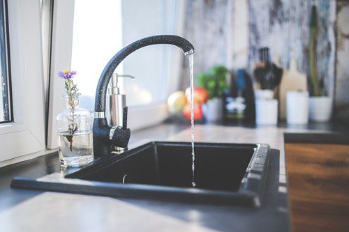 Modern kitchen sink with running water and a small flower vase.