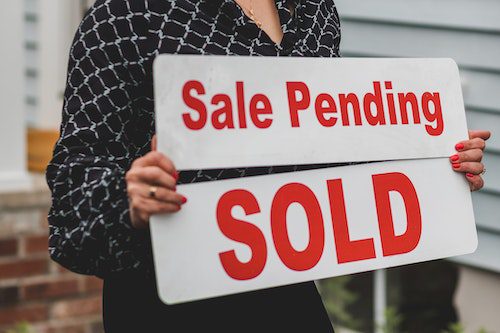 Person holding a sold sign with sale pending text.