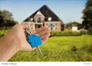 Hand holding house-shaped key in front of a suburban home.