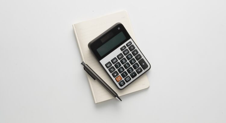 A calculator, notebook, and pen arranged on a white surface.