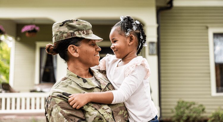 Soldier lovingly holding a smiling child outdoors.