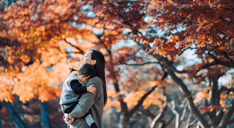 Mother holding child outdoors amid autumn leaves.