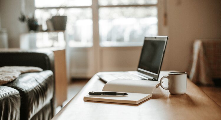 A minimalist workspace with a laptop, notebook, and pen on a wooden desk.