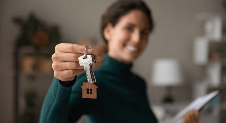 A person holding a house-shaped keychain with keys.