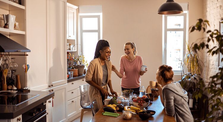 Three women enjoying cooking together in a sunny kitchen.