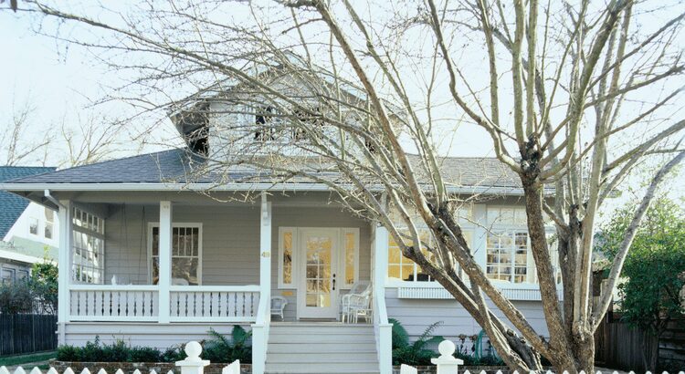A cozy gray house with a porch and leafless trees in front.
