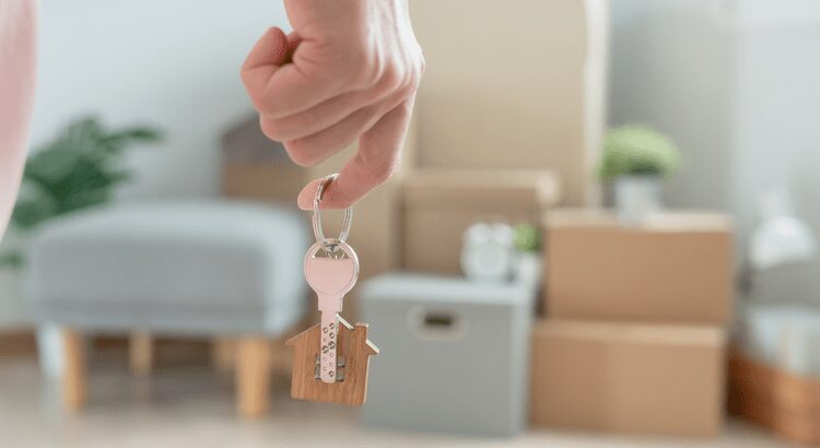 Hand holding a key with a house-shaped keychain in a living room.