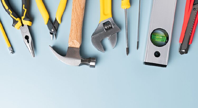 Various hand tools including a hammer, wrench, and pliers on a light blue surface.