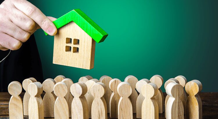 Wooden figures gather around a small wooden house with a green roof.