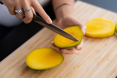 Person slicing a ripe mango on a wooden board.