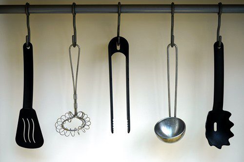 Three vintage kitchen utensils hanging on a rod.