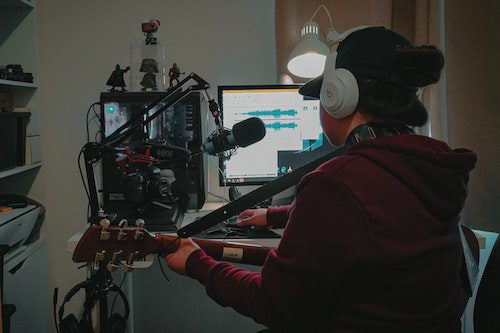 Person recording music in a home studio with guitar and microphone.
