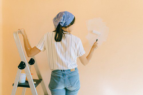 Woman painting a wall white with a roller.
