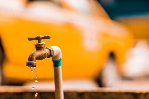Close-up of an outdoor water faucet with a blurred yellow vehicle in the background.