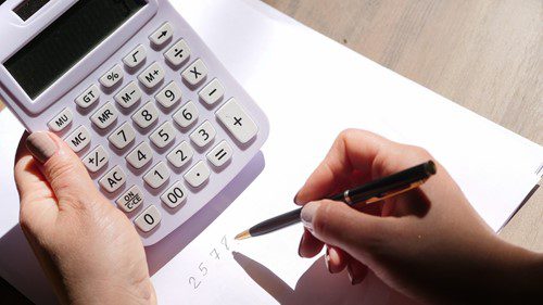 Person writing calculations beside a calculator.