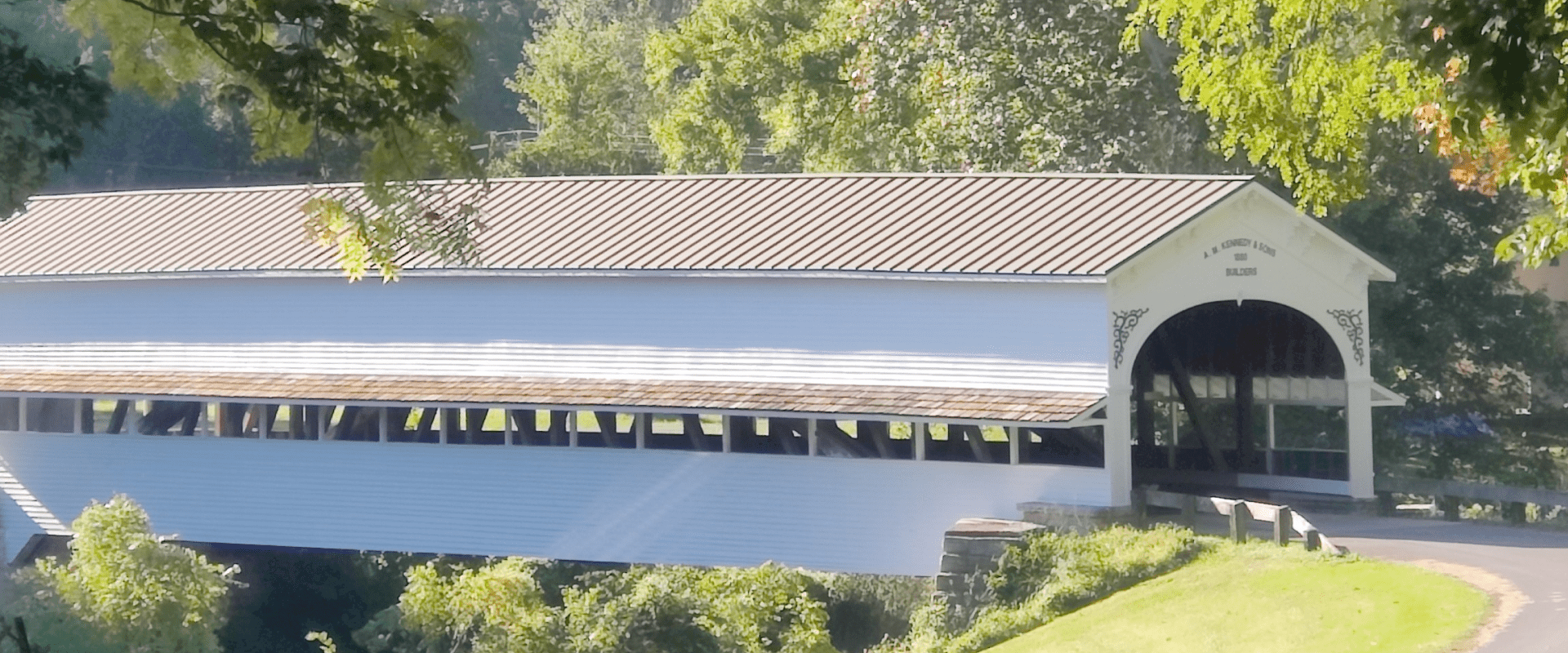 Covered wooden bridge over a river surrounded by greenery.