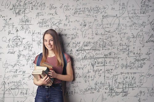 Young woman standing with books in front of a math-filled whiteboard.