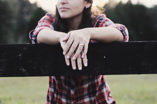 Person leaning on a fence with focus on hands and rings.