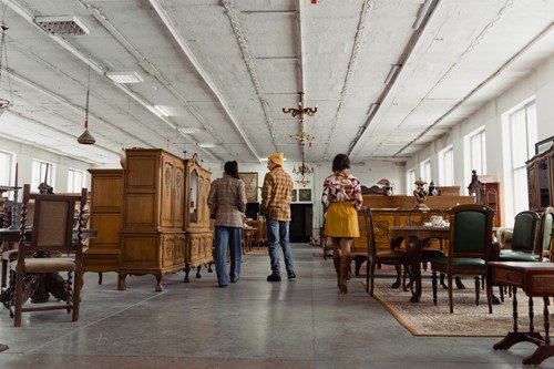 Three people exploring a spacious antique furniture store.