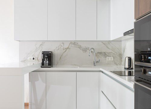 Modern white kitchen with marble backsplash and coffee machine.