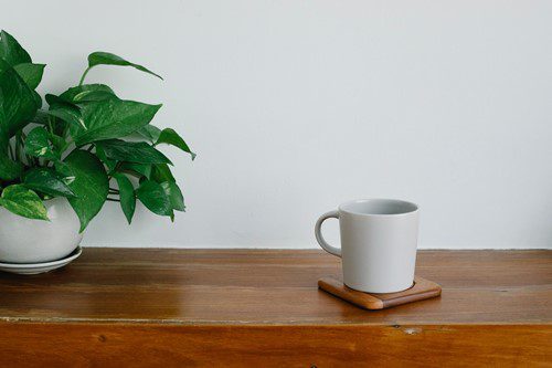 A white ceramic mug on a wooden table with a green plant beside it.