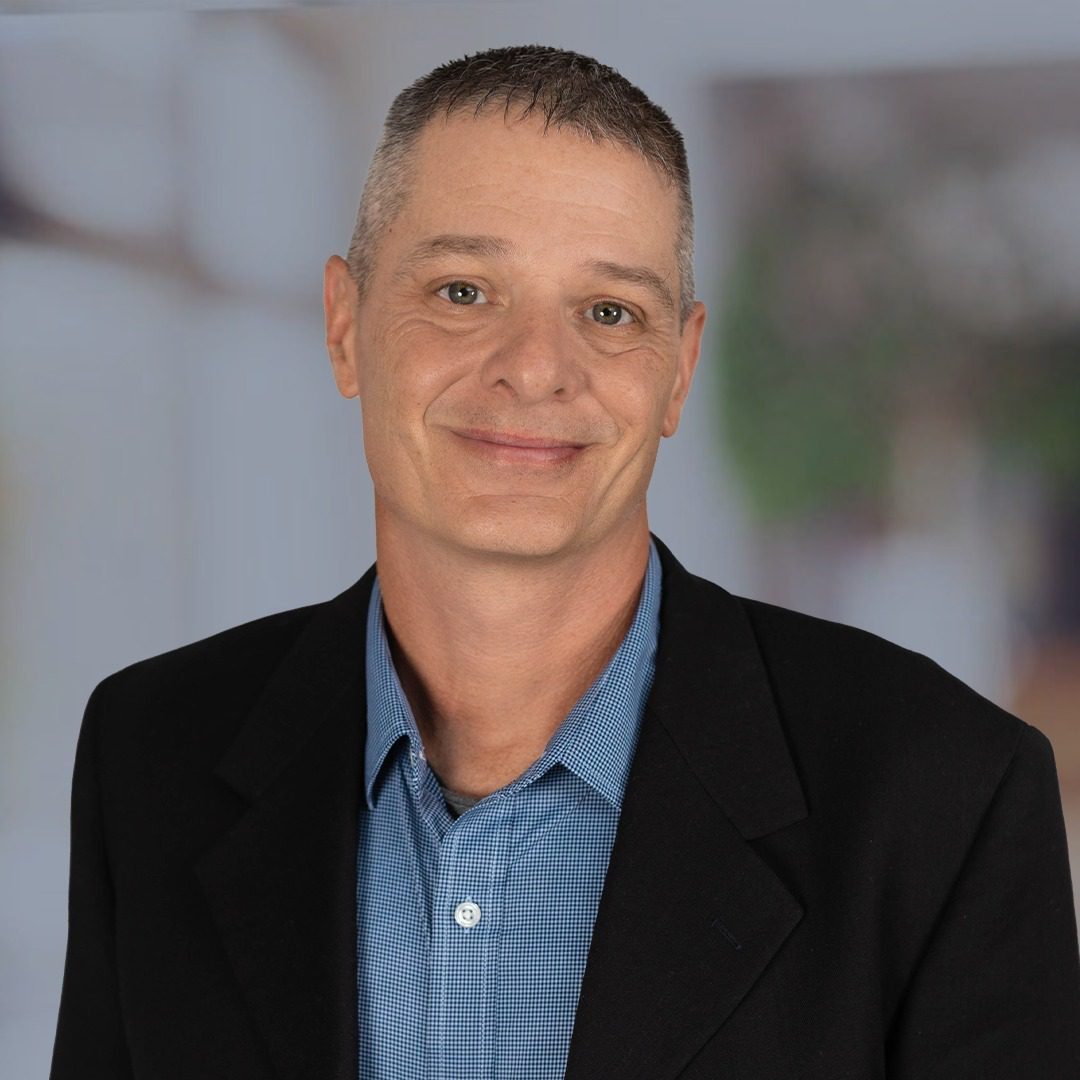 Professional man in a black blazer and blue shirt smiling.
