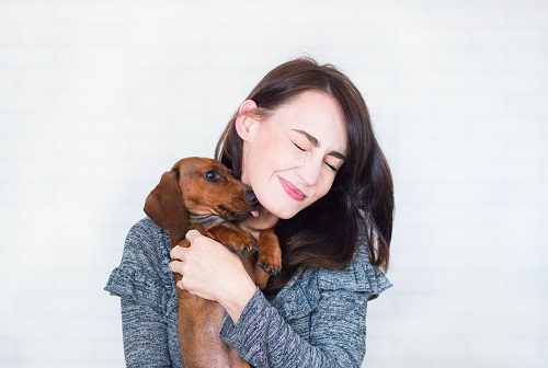 Woman happily hugging a small brown dog with eyes closed.