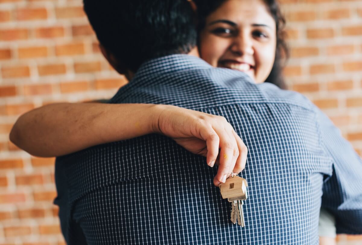 elevate-tips-moving A woman smiling while holding a key behind a man's back as they hug.